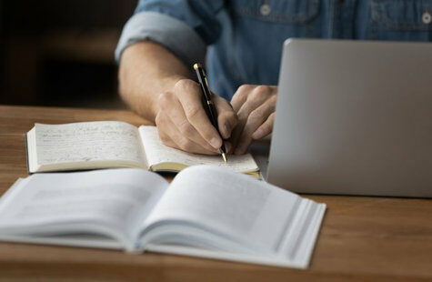 Person som sitter vid en dator och skriver i en anteckningsbok